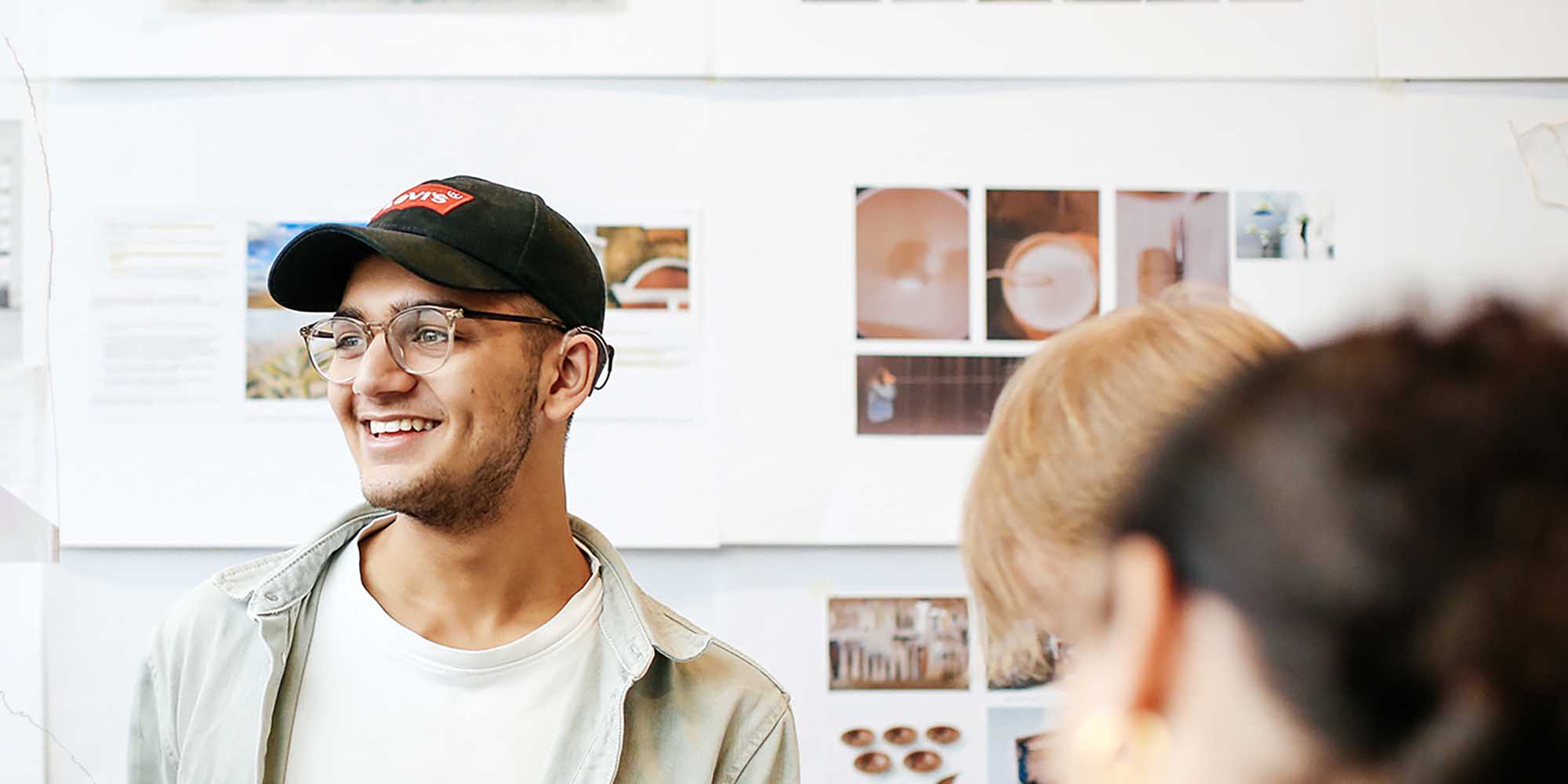 A student smiling. Behind him a white board with a collage of images