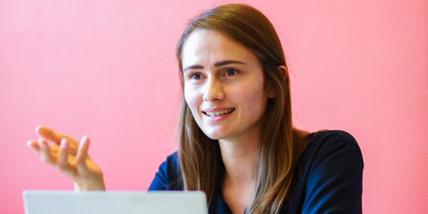 An image of a student engaged in conversation and sat behind her laptop.