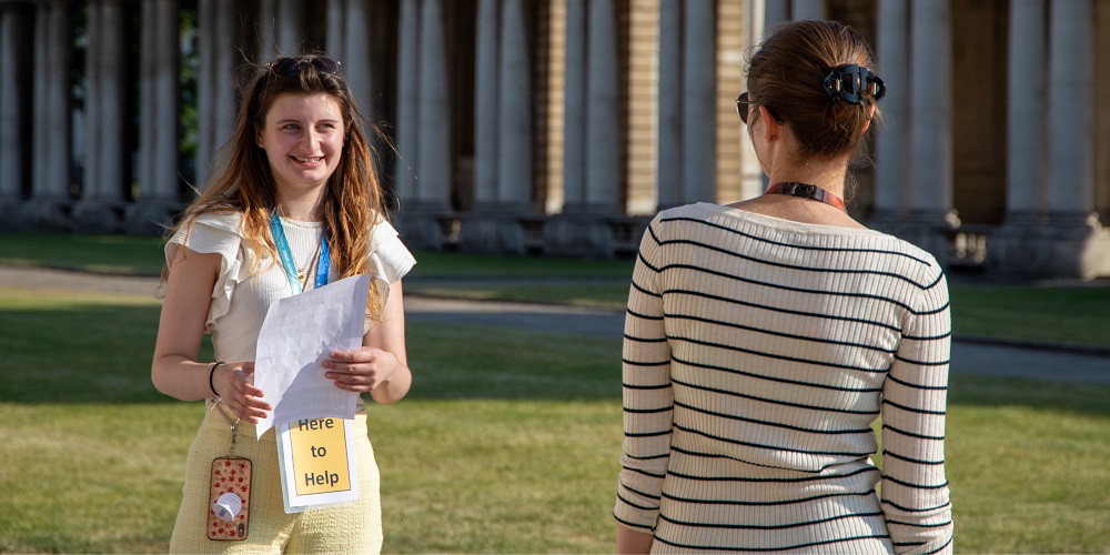 An image of two students helping at an event, one is facing the camera and smiling.